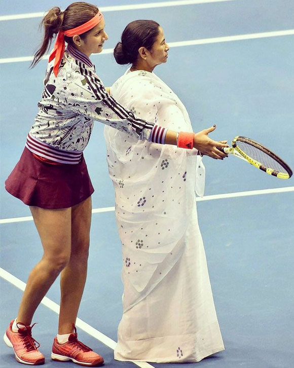West Bengal Chief Minister Mamata Banerjee gets a lesson in tennis from Sania Mirza before an exhibition match at the Netaji Indoor Stadium in Kolkata on November 25