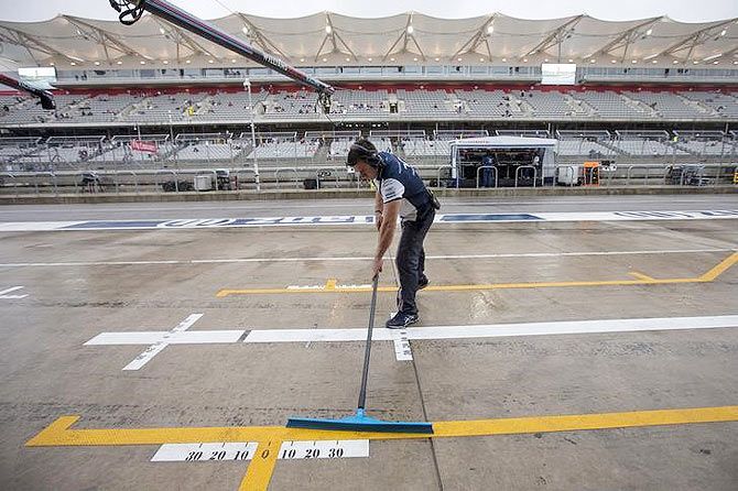 A Williams Formula One pit crew member clears rain water from pit lane ahead of the first practice session of the US F1 Grand Prix at the Circuit of The Americas in Austin, Texas on Friday