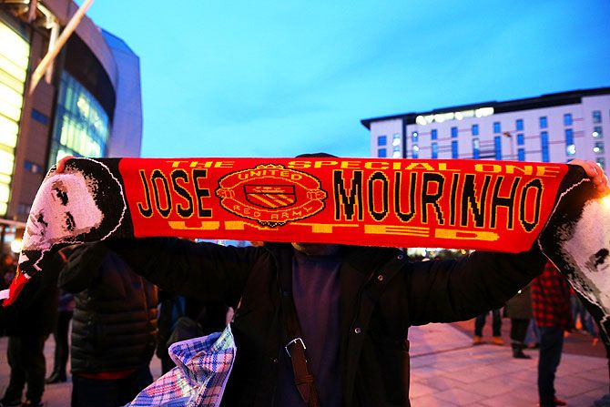 A fan poses with a Manchester United scarf displaying the image and name of Jose Mourinho, outside the stadium