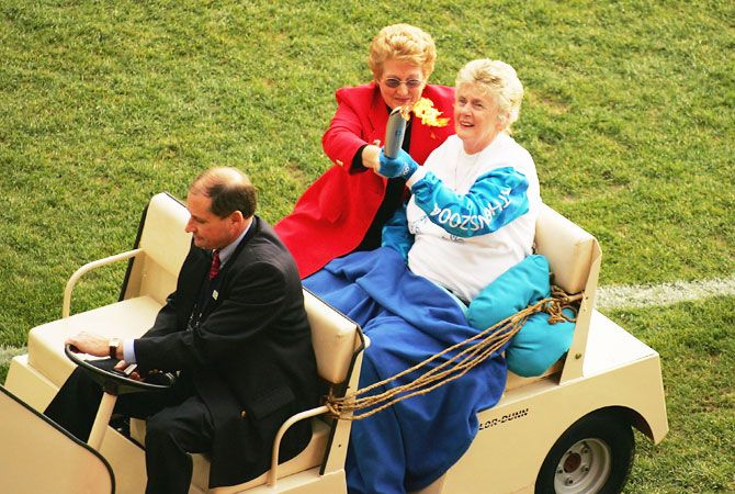 Betty Cuthbert of Australia is taken around the ground in a golf cart as she carries the olympic torch in the round eleven AFL match between the Hawthorn Hawks and the Essendon Bombers at the Melbourne Cricket Ground June 5 2004 in Melbourne, Australia