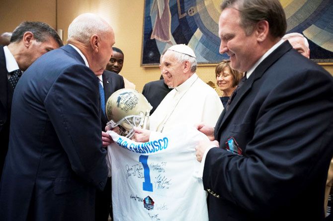 Pope Francis is presented with an American football helmet and a jersey during a meeting with members of American Pro Football Hall of Fame at the Vatican on Wednesday