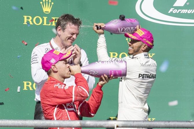 Mercedes driver Lewis Hamilton pours champagne on Mercedes technical director James Allison as Ferrari driver Sebastian Vettel (5) sips the bubbly on the podium after the United States Grand Prix. 