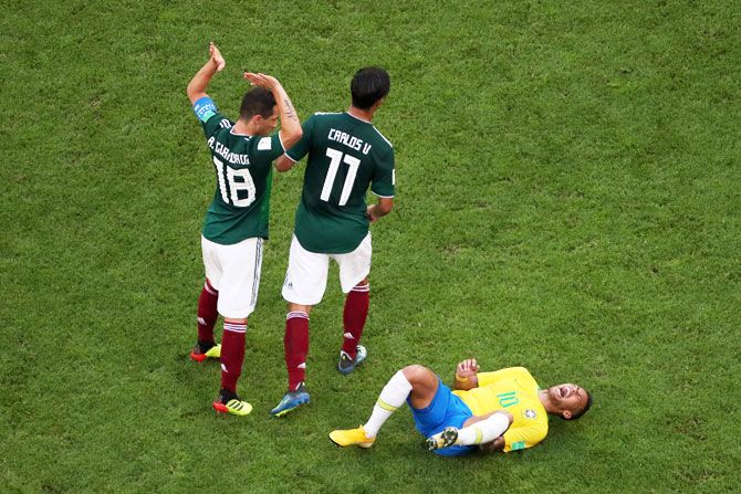 Neymar Jr of Brazil lies on the pitch injured while Andres Guardado and Carlos Vela of Mexico pass by