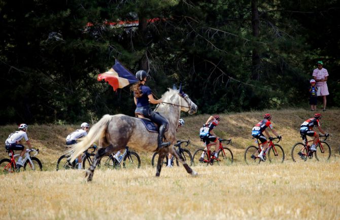 A woman on a horse carries the French flag on Bastille Day as the peloton passes by at the 181-km Stage 8 from Dreux to Amiens Metropole on July 14