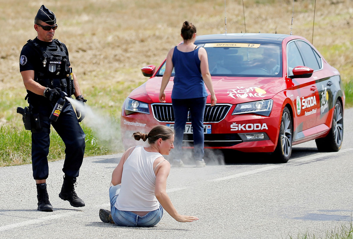 A police officer pepper sprays a protester as another protester stands in front of the race director's car during the 218-km Stage 16 from Carcassonne to Bagneres-de-Luchon on July 24