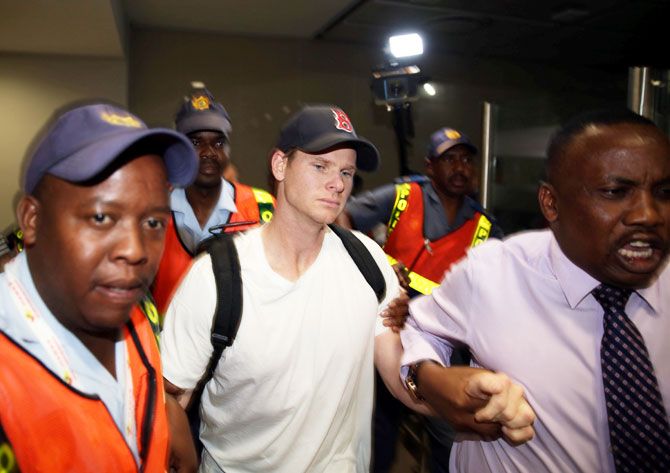 Axed Australian cricket captain Steve Smith is escorted by Police officers as he leaves the O.R. Tambo International Airport in Johannesburg on Wednesday