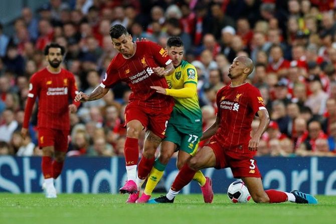 Norwich City's Emiliano Buendia makes a strong challenge to stop Liverpool's Fabinho and Roberto Firmino.