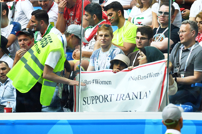 A steward talks to fans displaying a banner referencing Iranian women during the match during a 2018 World Cup match between Morocco and Iran 