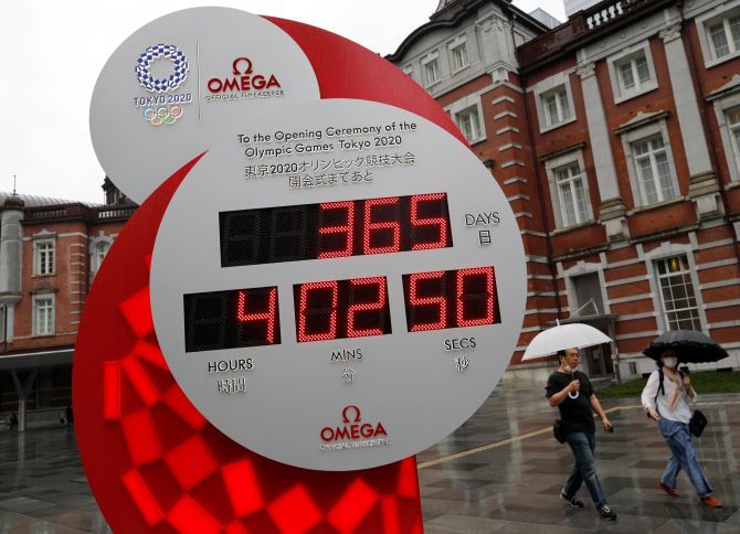 Passersby wearing protective face masks walk past a countdown clock for the Tokyo 2020 Olympic Games, on the day to mark the one-year countdown to the summer games that have been postponed to 2021 due to the coronavirus disease (COVID-19) outbreak, in Tokyo, on Thursday