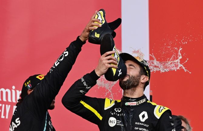 Third placed Daniel Ricciardo of Renault drinks out of a shoe as race winner Lewis Hamilton of Mercedes pours champagne over his head on the podium.