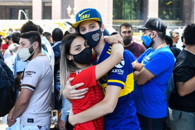 Fans of opposing Argetine clubs Boca Juniors and River Plata hug as they queue to enter the Casa Rosada where the body of Diego Maradona lays in state