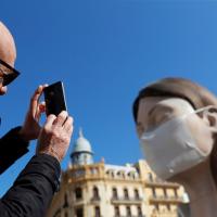 A man takes pictures of a monument displayed with a protective mask amid the COVID-19 pandemic