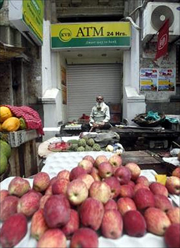 A roadside vendor selling fruits sits in front of a closed ATM counter during a two-day strike in Kolkata.