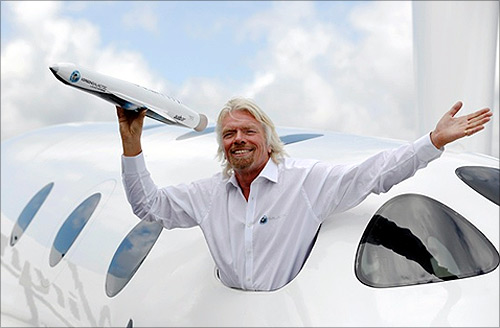 Richard Branson waves a model of the LauncherOne cargo spacecraft from a window of an actual size model of SpaceShipTwo on display.