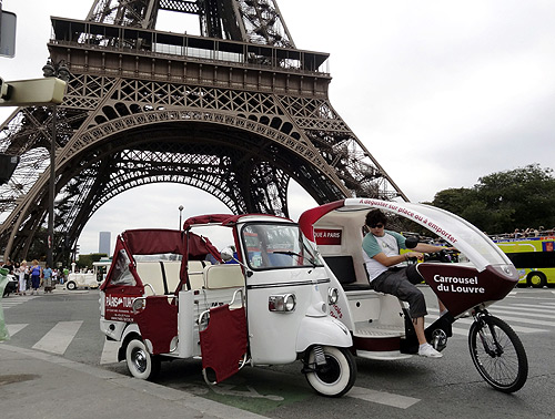 A velo taxi (R), or bicycle taxi, drives past the Eiffel Tower in Paris.