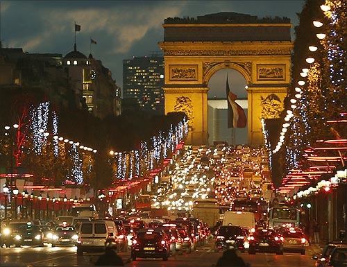 Christmas holiday lights hang from trees to illuminate Champs Elysees in Paris as rush hour traffic fills the avenue leading up to the Arc de Triomphe.