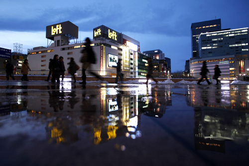 Pedestrians are reflected in a puddle in front of Sendai train station, Miyagi prefecture, northeastern Japan.