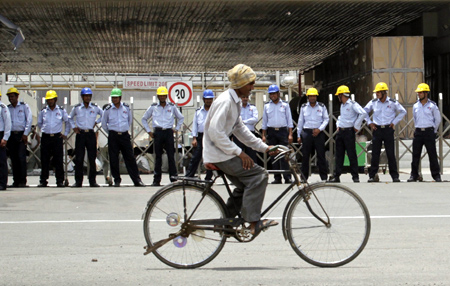 A man rides his bicycle past private security guards standing outside the main entrance to the Maruti Suzuki India.