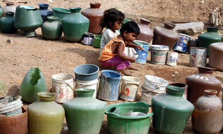 Children sit beside empty plastic cans used to collect water from a tap on the outskirts of Bangalore.