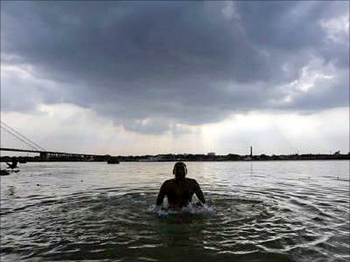 A devotee takes a dip against the backdrop of rain clouds in the river Ganga in Kolkata.