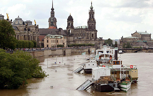 Boats are sen floating above the piers on a flooded street in front of the historic skyline of Dresden, along the banks of the river Elbe.