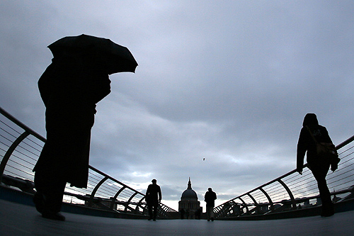 Commuters cross the Millenium Bridge during a rainy morning, towards the financial district the City of London.