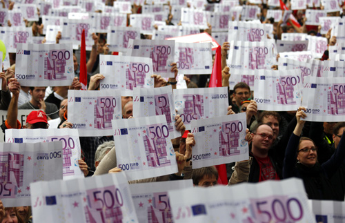 Demonstrators hold up large cardboard 500 euro notes and a sign reading fair sharing - taxes for the rich during an anti-capitalism protest in Frankfurt.
