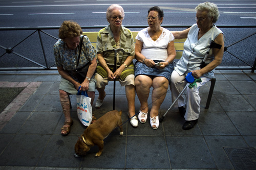 A group of women sit on a bench in the shade on a hot summer evening in Madrid.