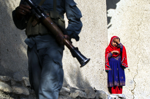 An Afghan girl watches as a member of the Afghan Uniformed Police walks past with paratroopers from Chosen Company of the 3rd Battalion (Airborne), 509th Infantry.