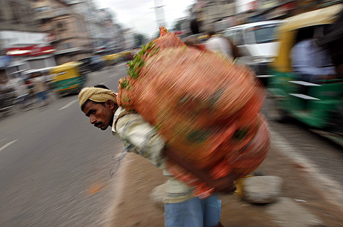 A labourer carrying a sack of vegetables waits to cross a road in the old quarters of Delhi.