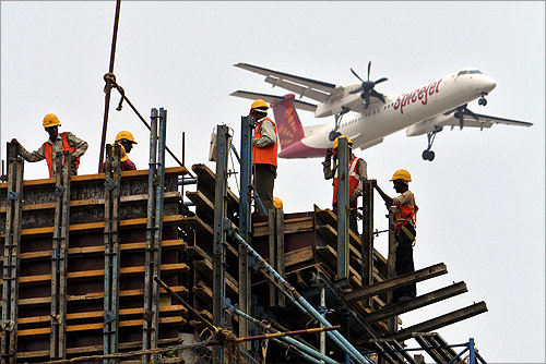 Construction workers erect scaffolding at the site of metro station as a SpiceJet Airlines aircraft flies past in Chennai.