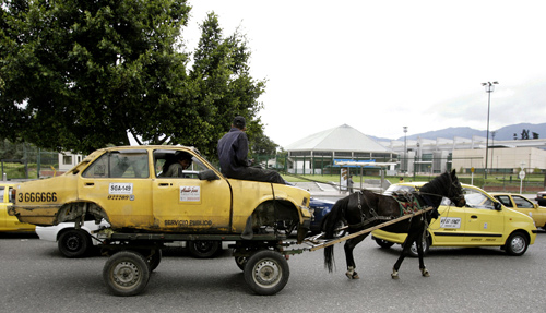 The remains of a taxi are transported by two men on a horse drawn cart on a main street of Bogota, Colombia.