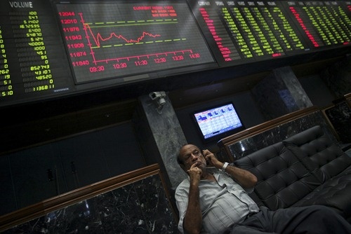 An investor talks on his mobile phone while sitting near an electronic board displaying stock prices at the Karachi Stock Exchange.