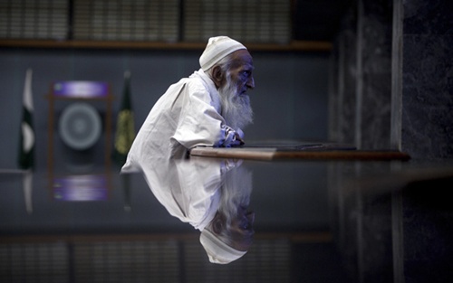 An elderly man is reflected on a marble table as he monitors share prices on a screen during a trading session at the Karachi Stock Exchange.