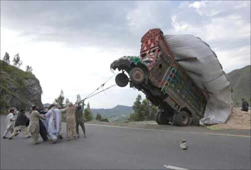 Men use ropes to try and right a supply truck overloaded with wheat straw, used as animal feed, along a road in Dargai, in the Malakand district, northwest of Pakistan's capital Islamabad.
