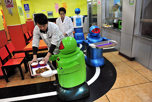 A robot that specialises in delivering food holds a tray as a waiter puts dishes on it at a Robot Restaurant in Harbin, Heilongjiang province.