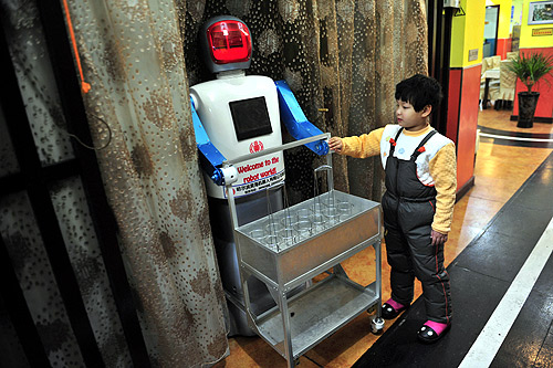 A boy touches a robot that specialises in delivering drinks at a Robot Restaurant in Harbin, Heilongjiang province.