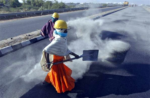 A woman labourer spreads black ash over a newly constructed road at Raipur village, in Gujarat.