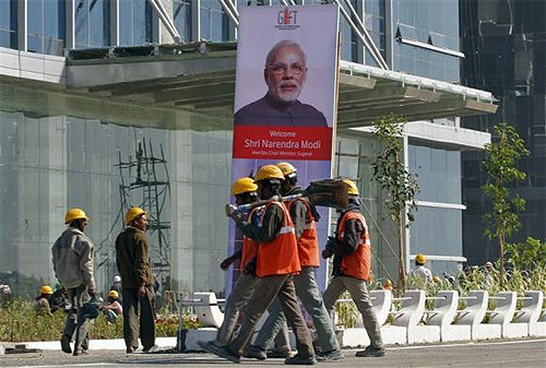 Workers walk past a poster of Gujarat's Chief Minister Narendra Modi installed at the construction site of Gujarat International Finance Tec-City (GIFT) building at Gandhinagar, in Gujarat.