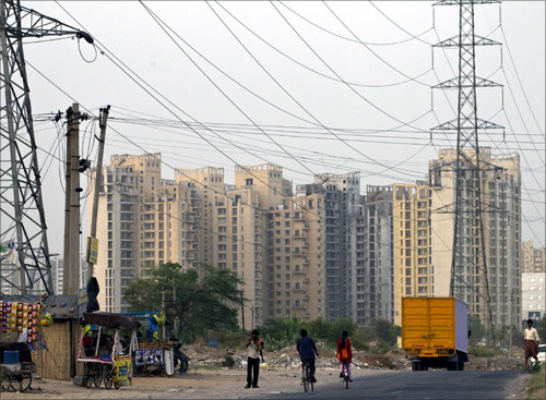 People ride their bicycles under overhead power cables, against the backdrop of multi-story residential apartments at Gurgaon.