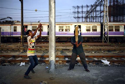 Boys play cricket along the tracks as a suburban train passes by, near Bandra railway station in Mumbai.