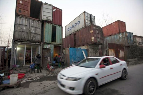 People stand outside shipping containers serving as their accommodation, as a car passes through a street, in Shanghai.