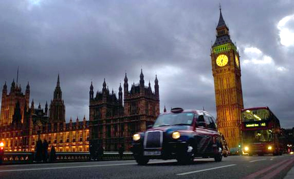 A bus and taxi pass Big Ben on Westminster Bridge in London.