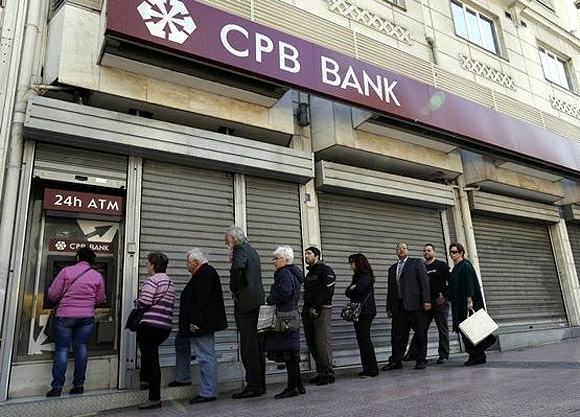 People queue up to make a transaction at an ATM machine outside a closed Cyprus Popular Bank (CPB) branch in Athens.
