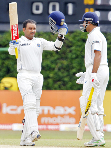 India's Virender Sehwag (left) raises his bat and helmet to celebrate his century as his teammate Vangipurappu Laxman watches