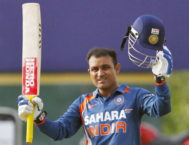 India's Virender Sehwag raises his bat and helmet to celebrate scoring his century against New Zealand