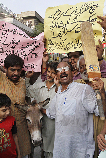 Pakistani cricket fans pose with a donkey as they hold placards and shout slogans against national players involved in a match fixing scandal in Lahore