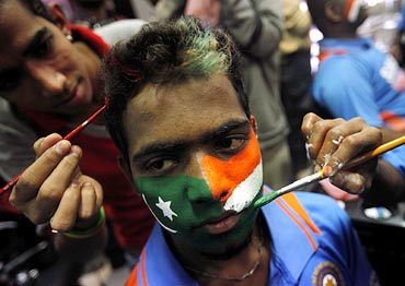 Face painters apply the colours of the Pakistani and Indian national flags to the face of a cricket fan in Mumbai