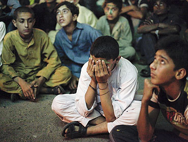 Young Pakistani cricket fans put on a dejected look after Pakistan's loss to India while sitting below a screen along a roadside in Karachi