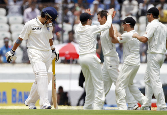 India's Sachin Tendulkar (L) walks back to the pavilion after being dismissed as New Zealand's Trent Boult (C) celebrates with teammates during the first day of their first test cricket match in Hyderabad